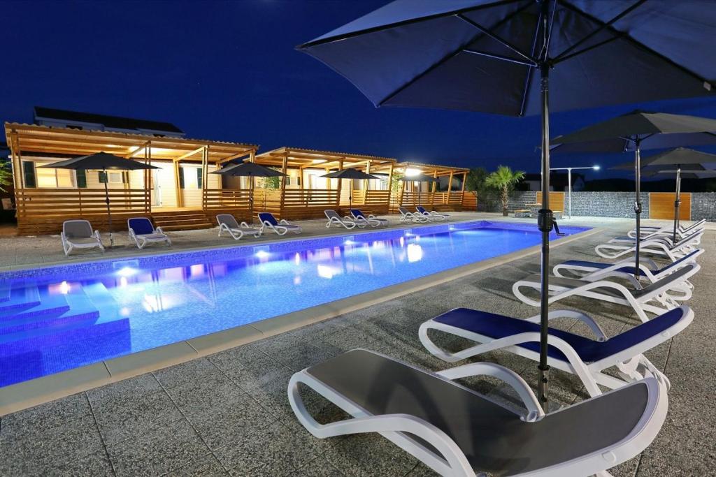 a pool with chairs and umbrellas at night at Mobillehome Camp Turanj in Turanj