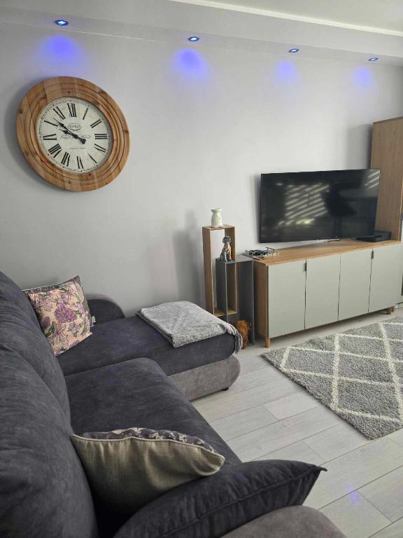 Una sala de estar con un sofá y un reloj en la pared. en Bee Happy Apartament Wrzesnia, en Września