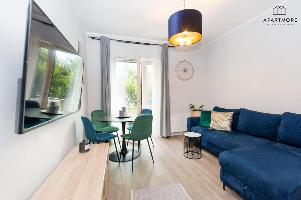 Compact living room with blue sectional, round dining table, green chairs, wall-mounted TV.