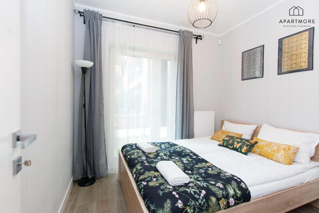 Bright bedroom with double bed, patterned throw, decorative pillows and rolled towels on top.