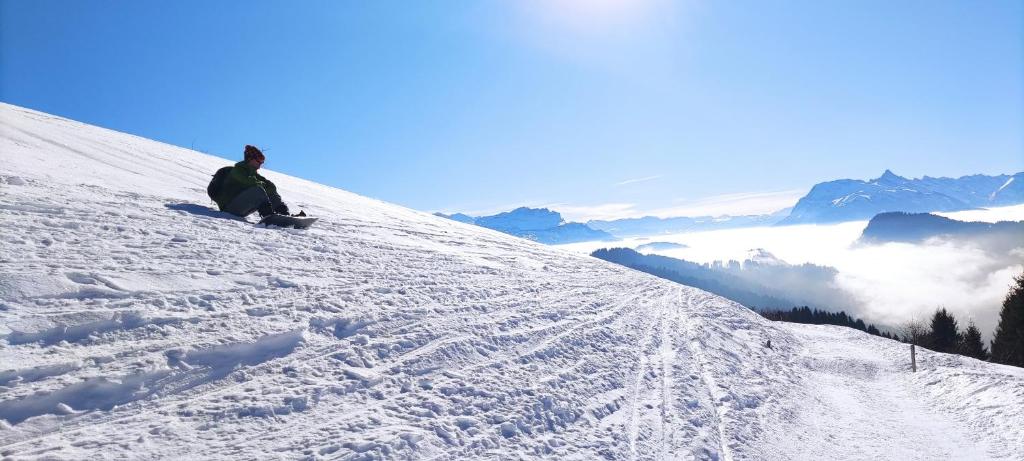 a person sitting on a snowboard on a snow covered slope at Les Gets apartment in Les Gets