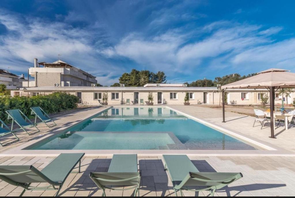 a swimming pool with chairs and an umbrella at Villa Lea in Pulsano