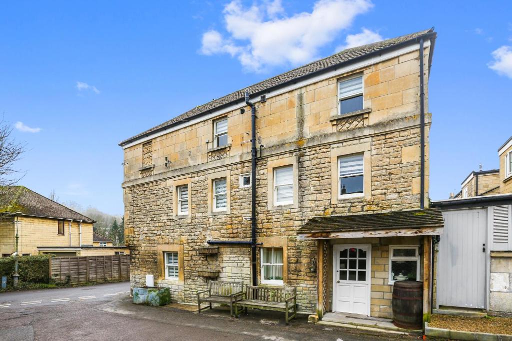 Un viejo edificio de ladrillo con un banco delante. en Charming 4-Bed Countryside Retreat with Parking, en Batheaston