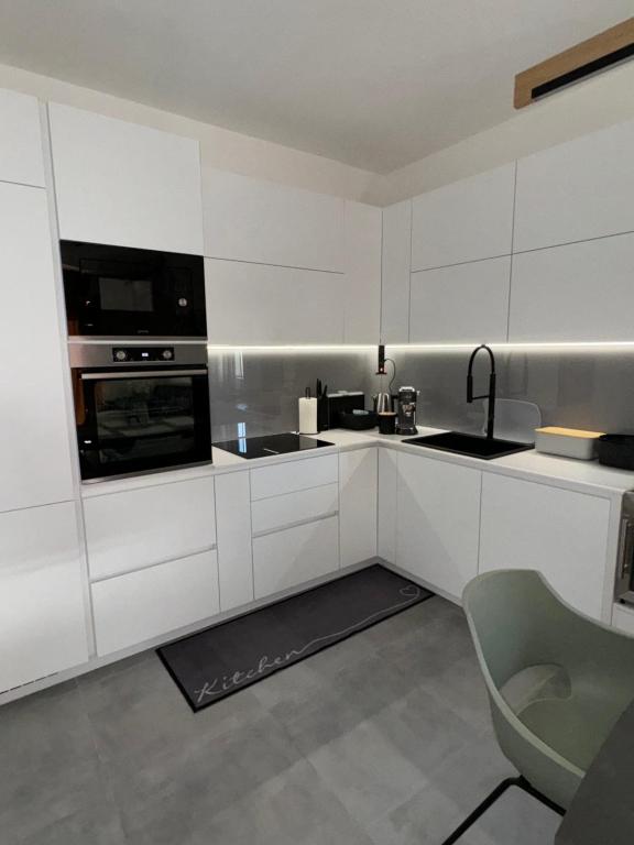 La cuisine est équipée de placards blancs, d'un évier et d'une chaise. dans l'établissement Studio apartman Mango, à Jadranovo