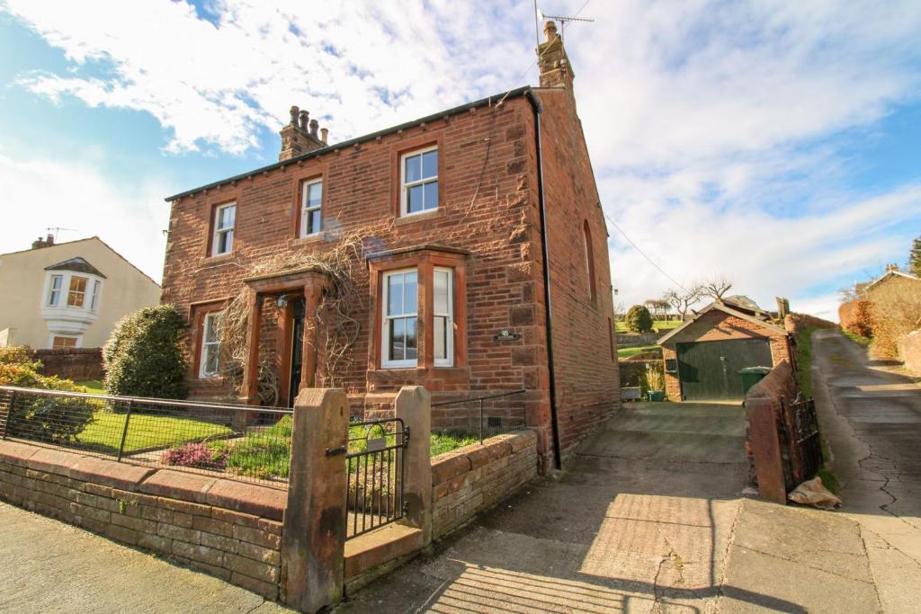 a brick house with a fence in front of it at Sunnyside, Lazonby in Lazonby