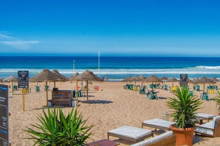 a beach with umbrellas and chairs and the ocean at Mountain View Beach House in Costa da Caparica
