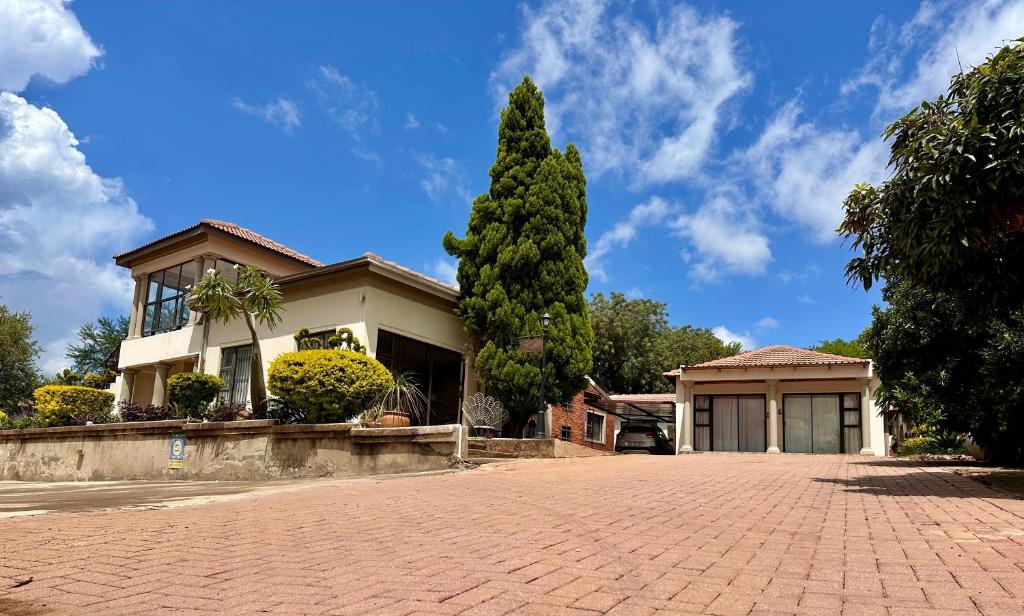 a house with a tree in front of a driveway at Dithabeng View Guest House in Rustenburg