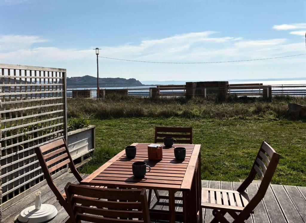 - une table et des chaises en bois sur une terrasse donnant sur la plage dans l'établissement Résidence Les Roches Blanches - Appartement vue mer terrasse et accès à la plage MAE-1101, à Trébeurden
