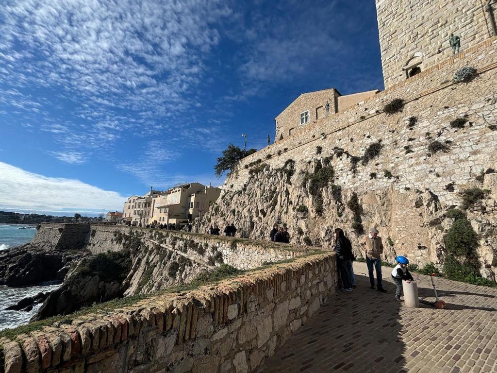 Un grupo de personas de pie en un muro cerca del océano. en Le Syracuse, en Antibes