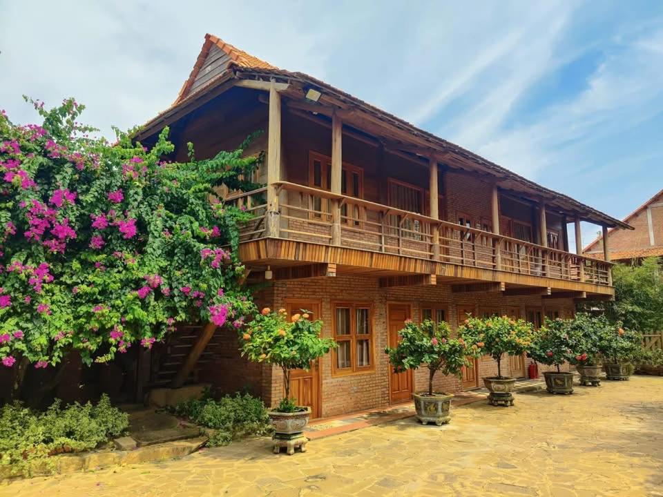 a wooden house with a balcony and some flowers at KND Wind Valley Bình Thuận in Xóm Chum Găng