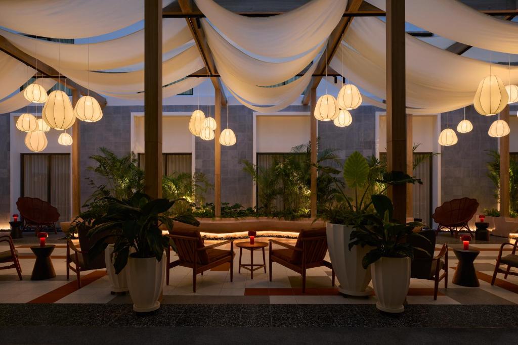 A softly lit lobby lounge arranged with armchairs, small tables, plants, and pendant lights.