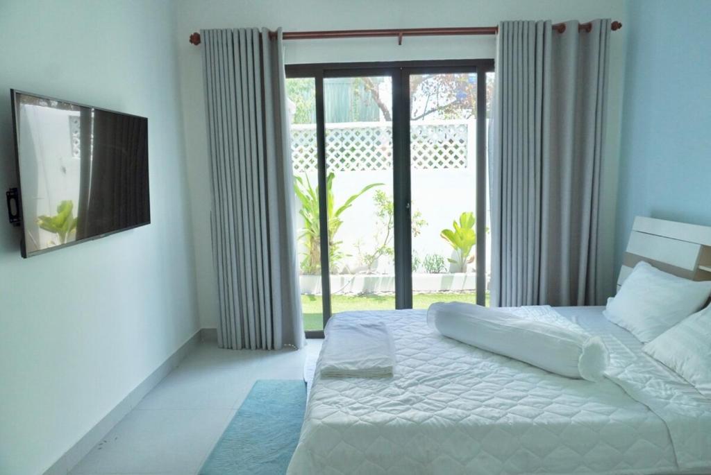 a bedroom with a white bed and a large window at Shin's House Cozy & Green Space in Phu Quoc
