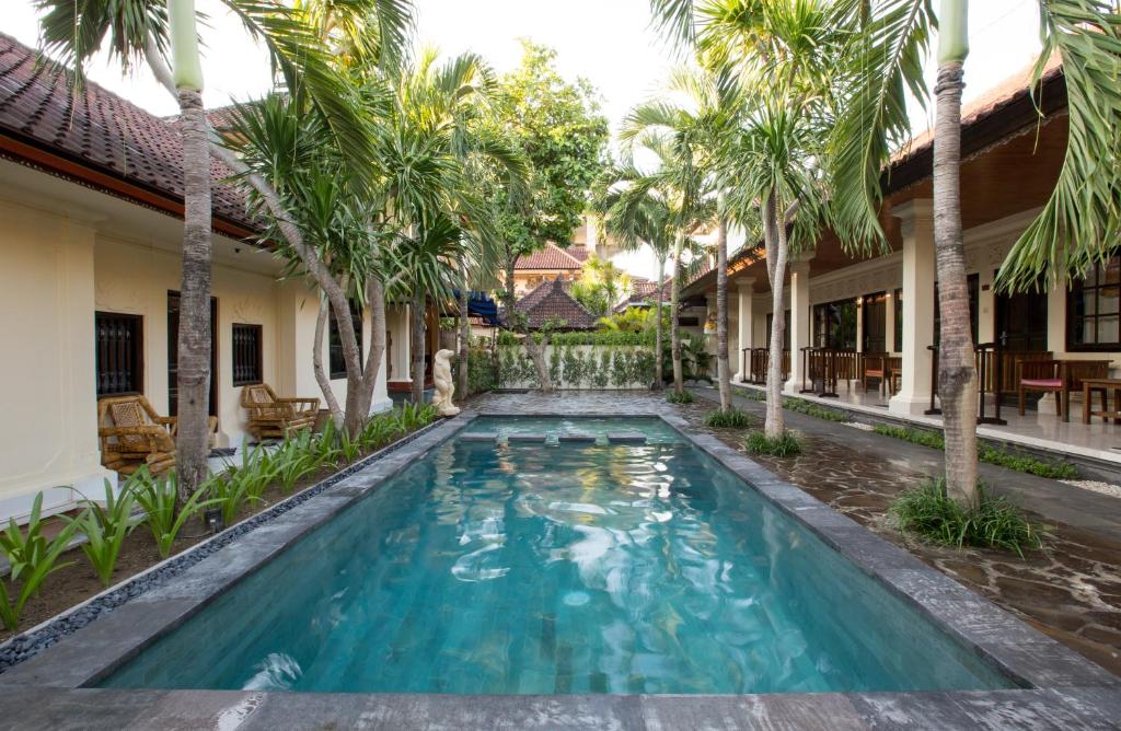 a swimming pool in the courtyard of a house with palm trees at Sari Indah Cottages in Kuta