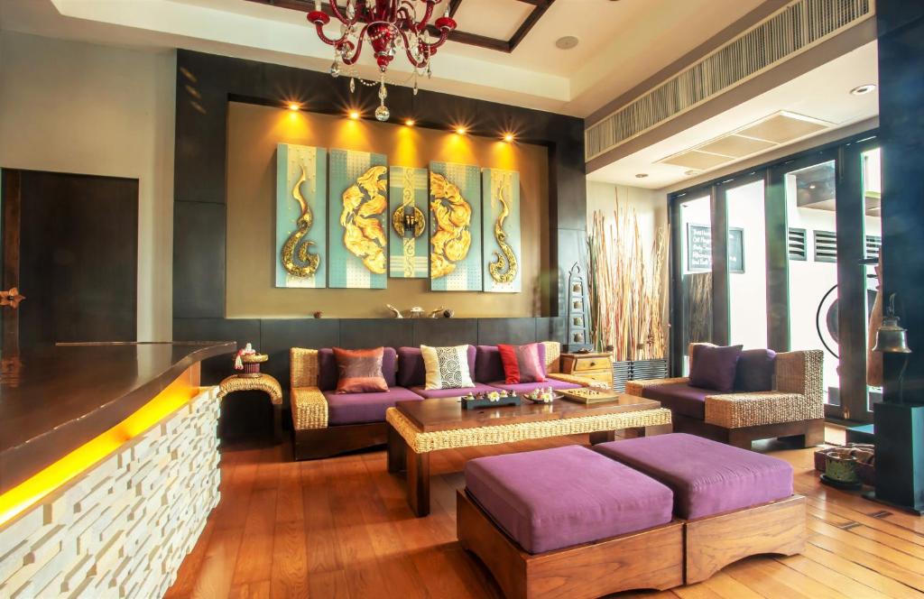 A richly decorated lounge with purple sofas, ottomans, dark wood and a red chandelier.