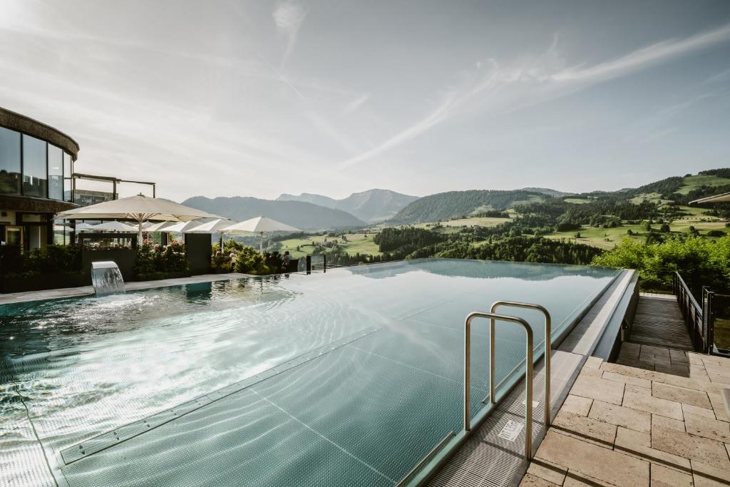 une grande piscine avec des montagnes en arrière-plan dans l'établissement Bergkristall - Mein Resort im Allgäu, à Oberstaufen