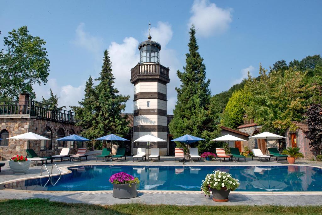 a swimming pool with a lighthouse in the background at Wineport Lodge Agva Riverside Hotel & Winery in Ağva