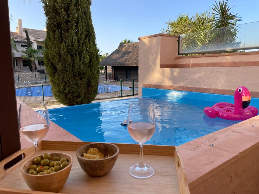 a table with two glasses of wine and a swimming pool at El oasis Monaco - 3 chambres in Fuente-Álamo de Murcia