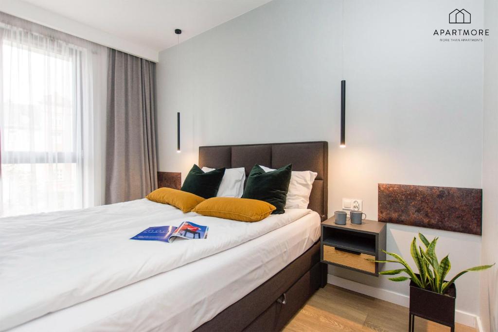 Bright bedroom with double bed, mustard and green cushions, pendant lights, bedside table and plant.
