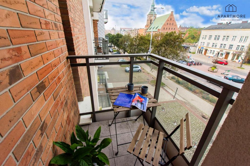 Small balcony with wooden folding table, two mugs and magazine, potted plant, street and church view.