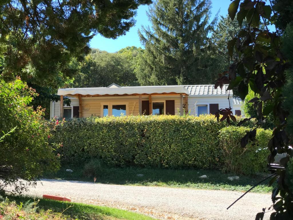 une petite maison derrière une haie devant une maison dans l'établissement CAMPING GINASSERVIS Mobile-home Flores, à Ginasservis