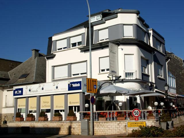 - un grand bâtiment blanc avec un parasol devant dans l'établissement Auberge La Veranda, à Luxembourg