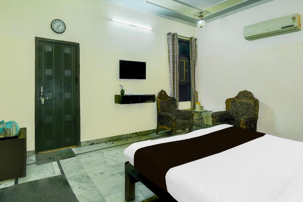 a bedroom with a bed and two chairs and a tv at Super Hotel O Sikar Road Jaipur Formerly Garg Niwas in Jaipur