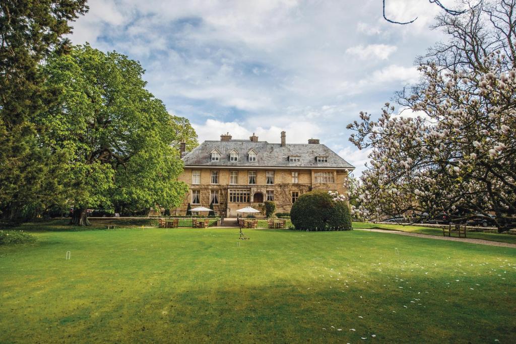 uma casa grande com um grande relvado em frente em The Slaughters Manor House em Lower Slaughter