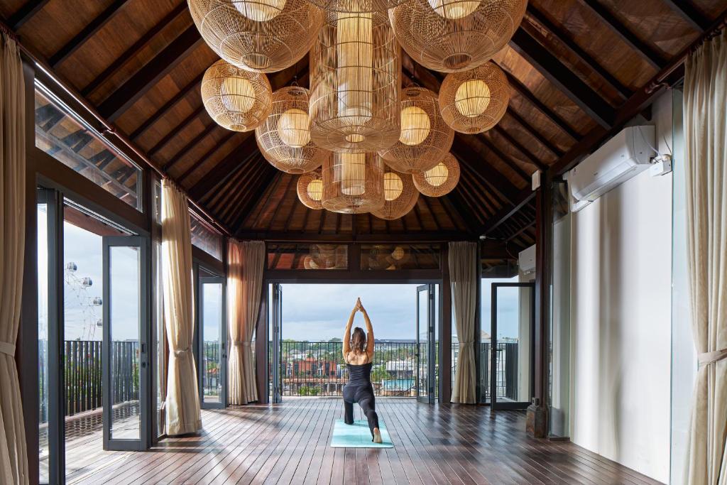 a woman standing on a yoga mat in a room with a chandelier at Aahana Village Bali in Canggu