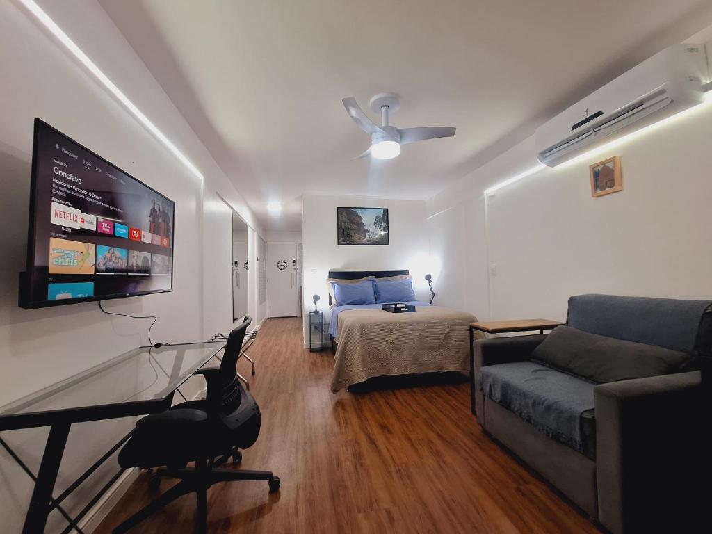 a living room with a couch and a bed and a flat screen tv at Studio tipuana, varandinha aberta com rede in Brasilia