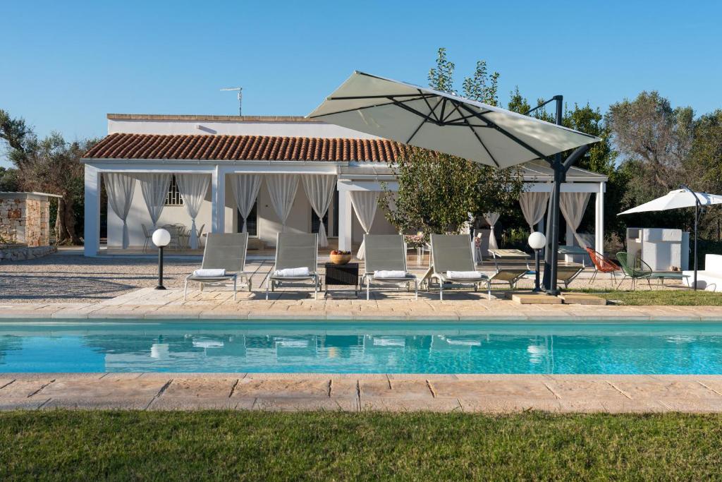 - un groupe de chaises et un parasol à côté de la piscine dans l'établissement Villa L'Ulivo by Bianco Puglia Vacanze, à San Vito dei Normanni