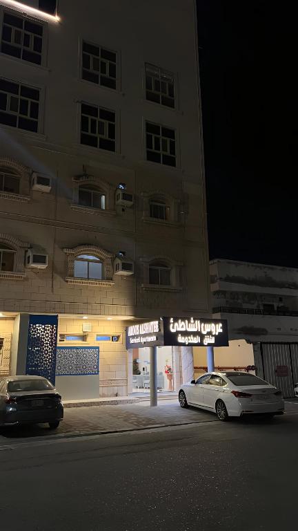 Dos coches aparcados delante de un edificio por la noche. en عروس الشاطئ للشقق المخدومة, en Umm Lajj