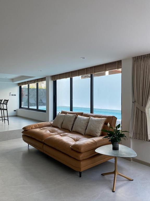 a brown leather couch in a living room with windows at Mountain breeze villa phuket in Ban Bang Khu