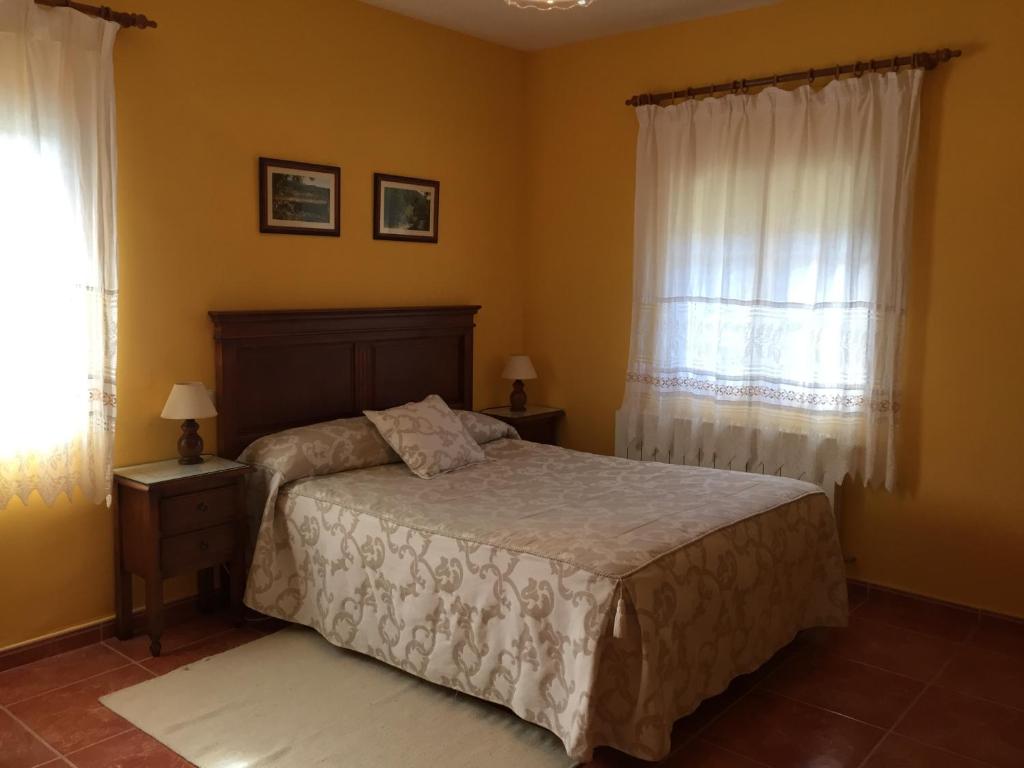 a bedroom with a bed and two windows at Casa Rural Sierra de Tormantos in Guijo de Santa Bárbara
