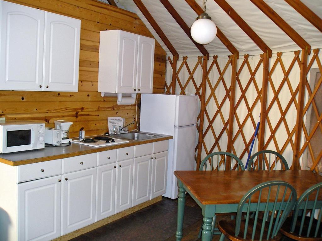 cocina con armarios blancos, mesa y nevera en Yosemite Lakes River Yurt 21 en Harden Flat