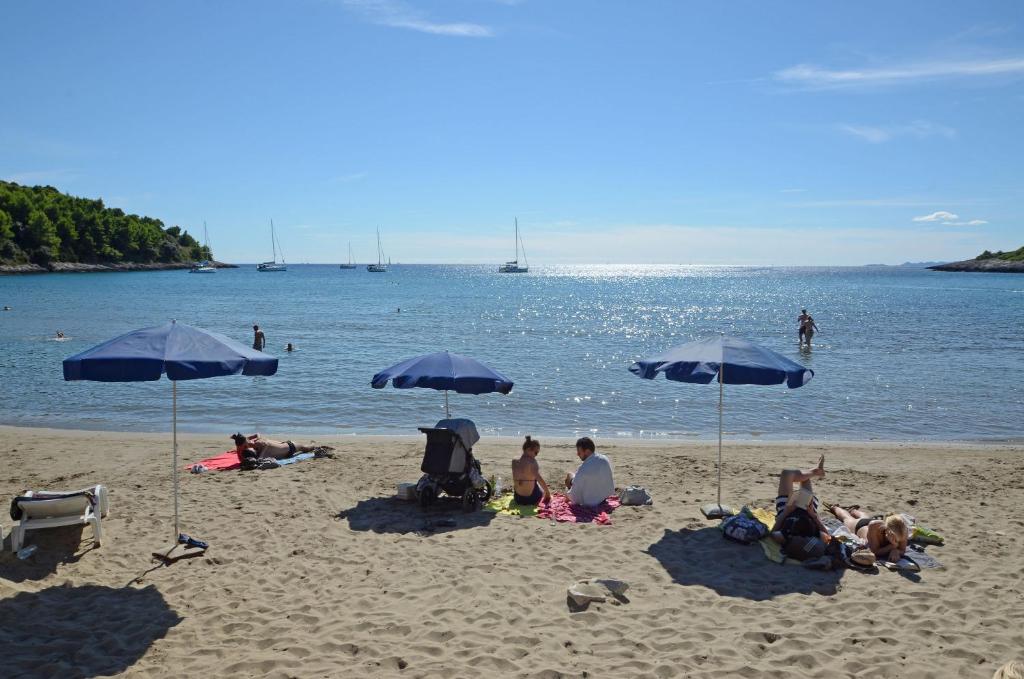 a group of people sitting on the beach under umbrellas at Apartments Željka in Lumbarda