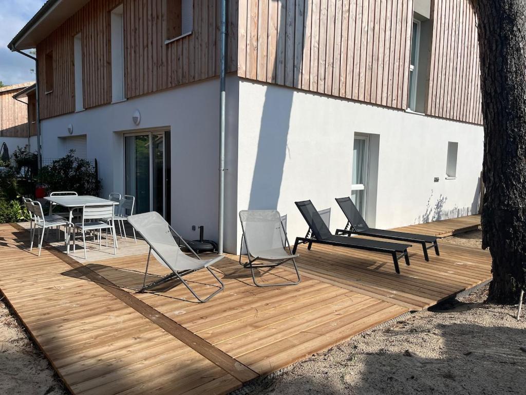 une terrasse en bois avec des chaises et une table. dans l'établissement Villa neuve 300 m plage sud 3 chambres, à Lacanau