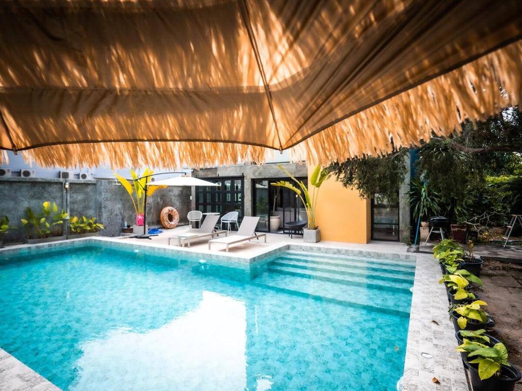 an outdoor swimming pool with a large wooden umbrella at Rare, Special Beach Pool Villa in Hua Hin
