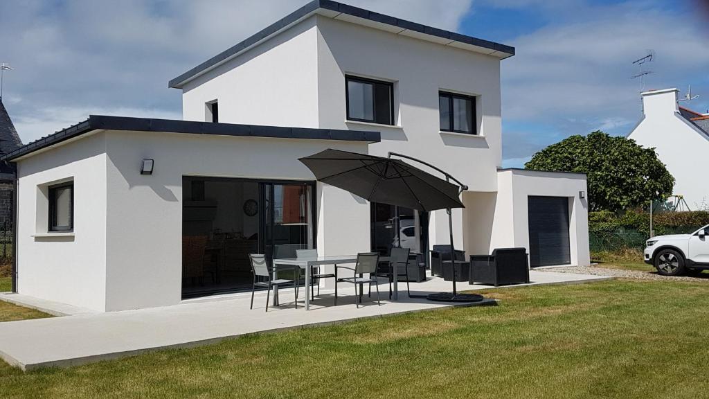 une maison blanche avec une table, des chaises et un parasol dans l'établissement Maison neuve 400 m des plus belles plages, à Loctudy