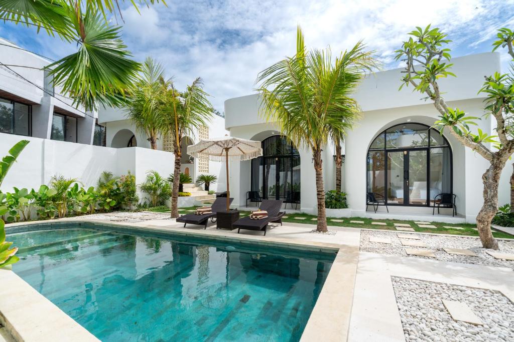 a pool with palm trees in front of a house at Tamanna Villa Uluwatu in Uluwatu