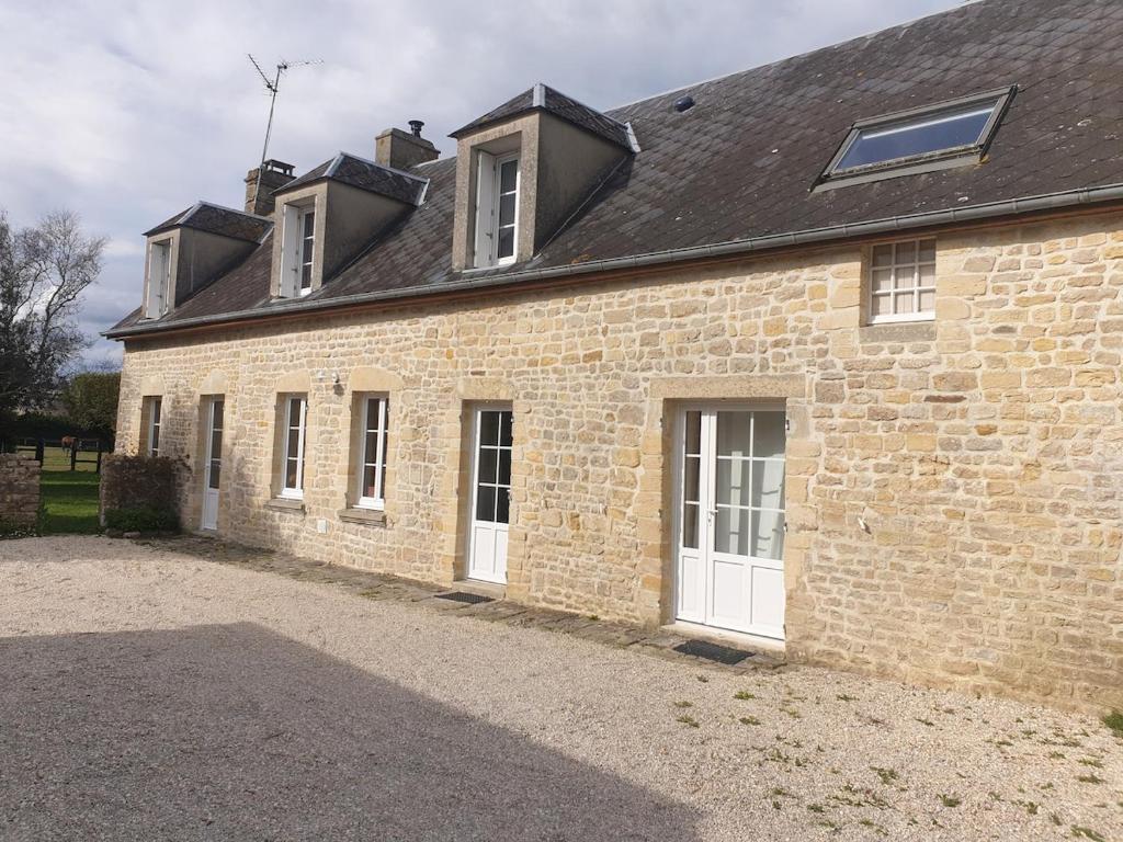 un bâtiment en briques avec des portes blanches et un toit dans l'établissement Jolie maison en pierre proche de la plage d'Omaha, à Vierville-sur-Mer