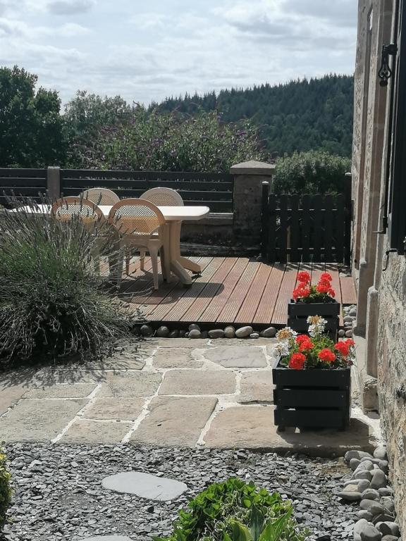 - une terrasse avec une table, des chaises et des fleurs dans l'établissement La Maison de Valie, à Mercoeur