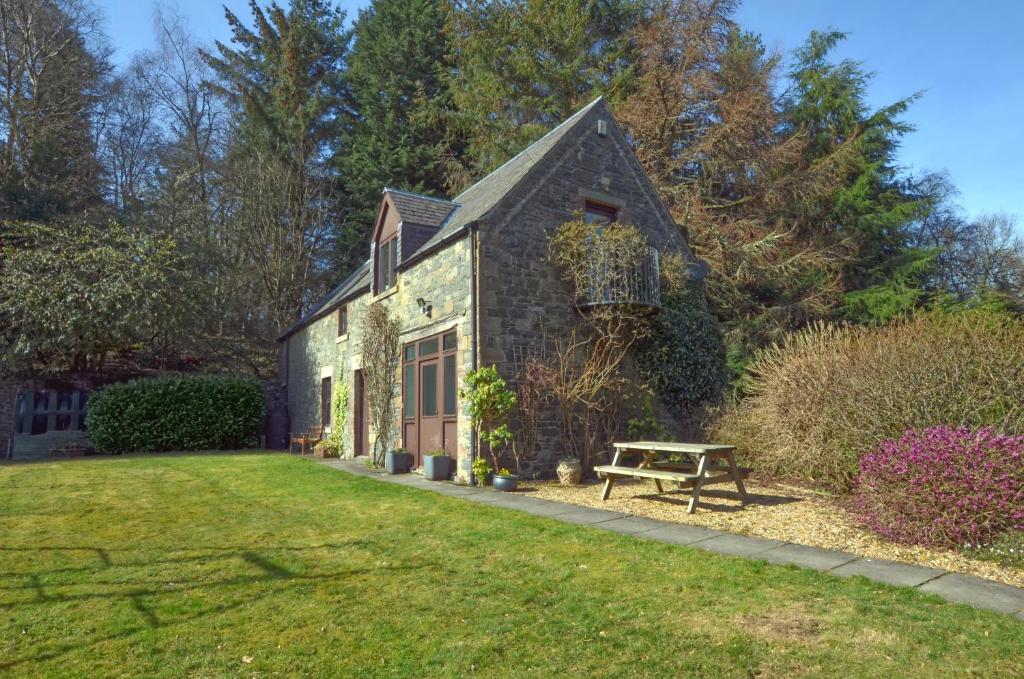 Black Barony Home Farm Cottage في إيدلستون: منزل حجري قديم مع مقعد في الفناء