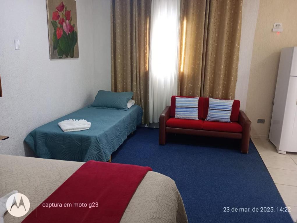 a room with two beds and a red chair at Kitnet Privativa no Portal de Campos do Jordão in Campos do Jordão