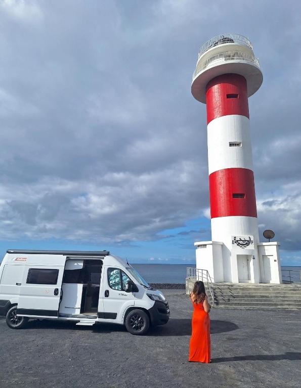a girl standing next to a van in front of a lighthouse at Camper La Palma fianza 600eu in Santa Cruz de la Palma