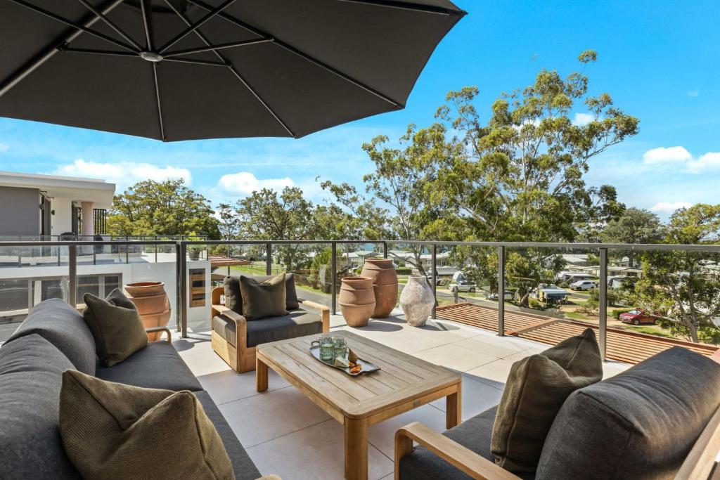 a patio with couches and a table and an umbrella at Oceanview Penthouse by Experience Jervis Bay in Huskisson