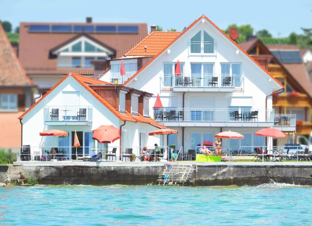 ein Gebäude mit Tischen und Sonnenschirmen neben dem Wasser in der Unterkunft Seehotel BelRiva in Hagnau