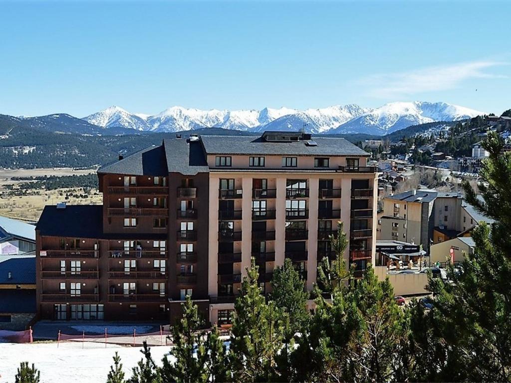 un grand bâtiment avec des montagnes enneigées en arrière-plan dans l'établissement Appartement au centre avec parking, 4 couchages - FR-1-593-129, aux Angles