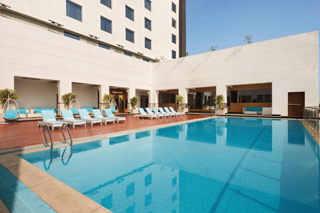 a swimming pool in a hotel with chairs and a building at Saura Hotel, Agra in Agra