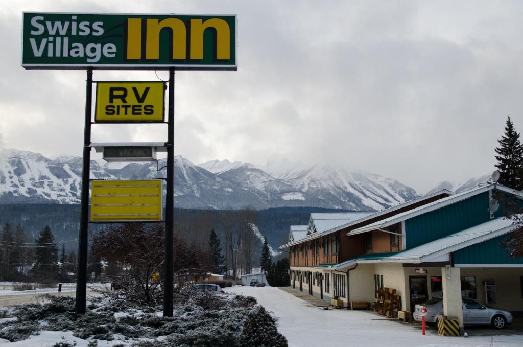 um sinal em frente a um edifício com neve no chão em Swiss Village Inn em Golden