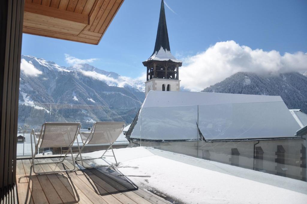 einen Balkon mit zwei Stühlen und eine Kirche mit einem Uhrturm in der Unterkunft Panoramic Ecodesign Apartment Obersaxen - Val Lumnezia I Vella - Vignogn I near Laax Flims I 5 Swiss stars rating in Vella